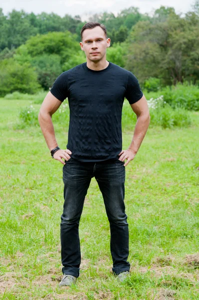 Человек в черной футболке стоит на траве — стоковое фото