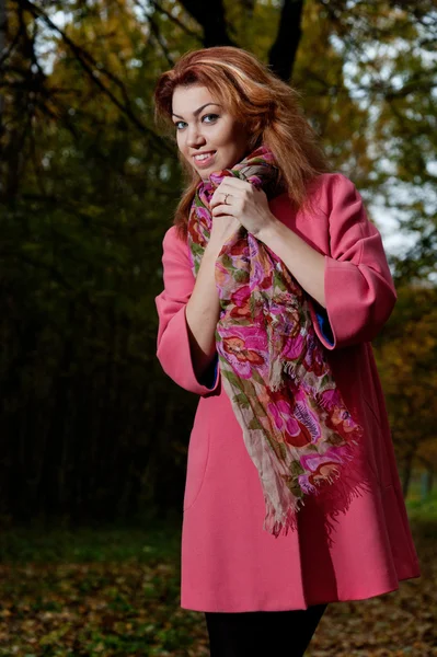 Vacker kvinna i rosa kappa promenader i parken — Stockfoto