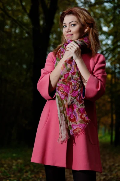 Vacker kvinna i rosa kappa promenader i parken — Stockfoto