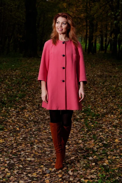 Schöne Frau in rosa Mantel spaziert durch den Park — Stockfoto