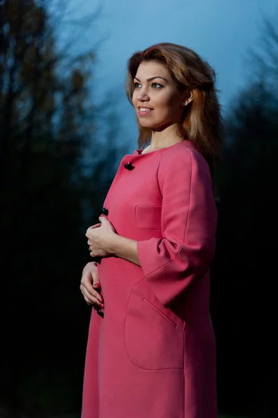 Mooie vrouw in roze vacht wandelingen in het park bij avond — Stockfoto