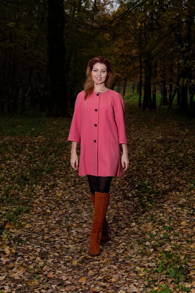 Schöne Frau in rosa Mantel spaziert durch den Park — Stockfoto