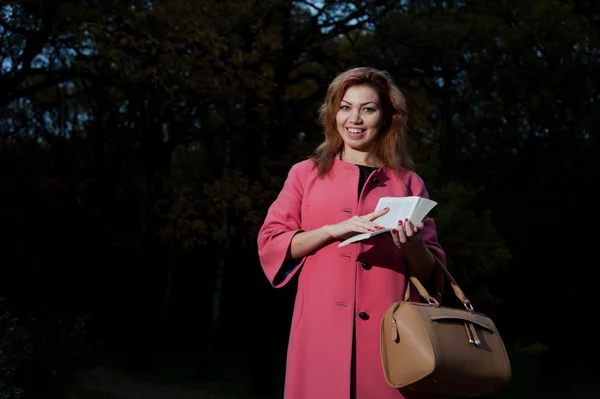 Hermosa mujer en abrigo rosa con paseos de libro en el Parque — Foto de Stock