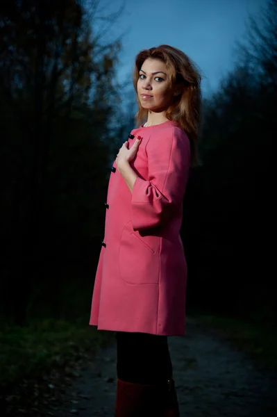 Bella donna in cappotto rosa passeggia nel parco la sera — Foto Stock