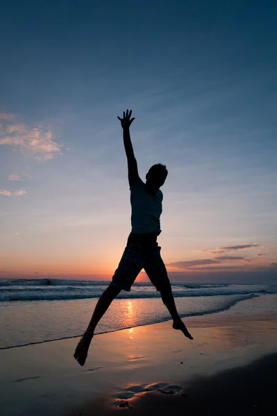 Man springen op het strand bij de zonsondergang — Stockfoto