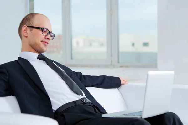 Улыбающийся бизнесмен сидит на диване с ноутбуком — стоковое фото