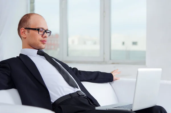 Young businessman sitting on couch with laptop — Stock Photo, Image