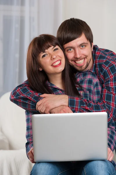Young laughing couple using laptop while sitting on couch at hom — Stock Photo, Image