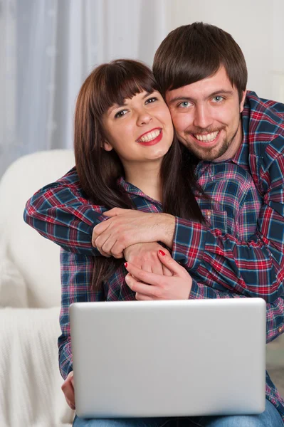 年轻笑的夫妻坐在沙发上使用便携式计算机 — 图库照片