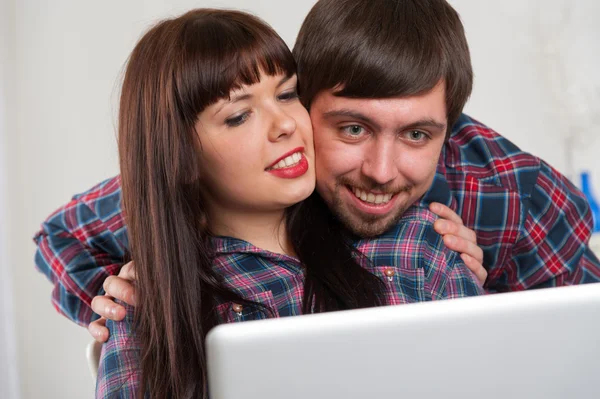 年轻的夫妇在家里使用的便携式计算机。男人拥抱的女人 — 图库照片