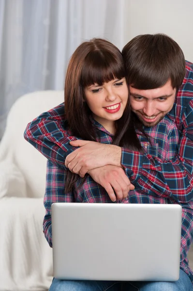 Portrait of young smiling couple using laptop while sitting at h — Stock Photo, Image