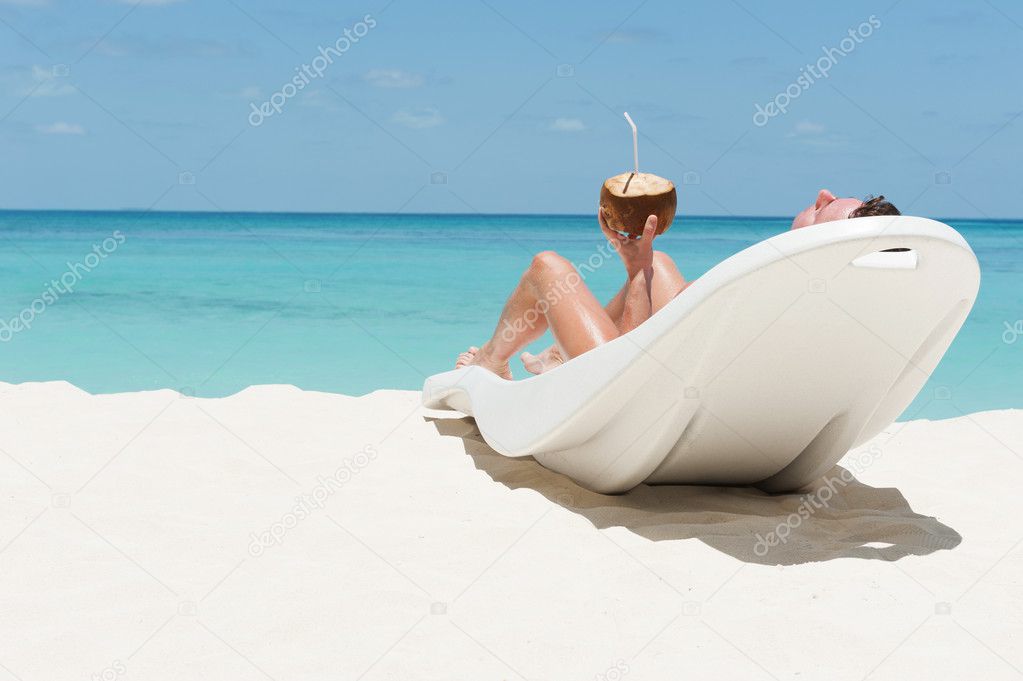 Man lie on lounger sunbed and drink coconut cocktail on beach wi