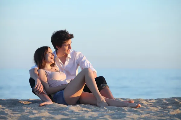 Pareja sentada y riendo en la arena de la playa al atardecer —  Fotos de Stock