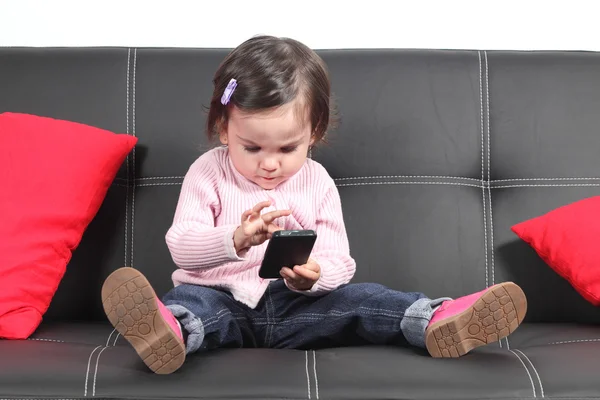 Casual baby sitting on a couch touching a mobile phone — Stock Photo, Image