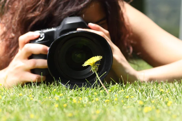 Gros plan d'une jolie fille prenant une photo d'une fleur sur l'herbe — Photo