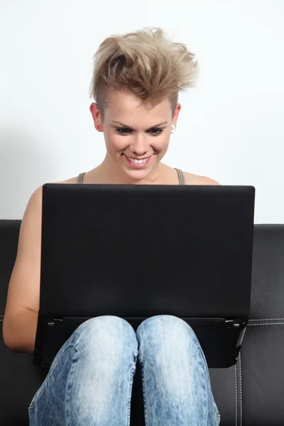 Fashion teenager girl sitting on a couch browsing in a laptop — Stock Photo, Image