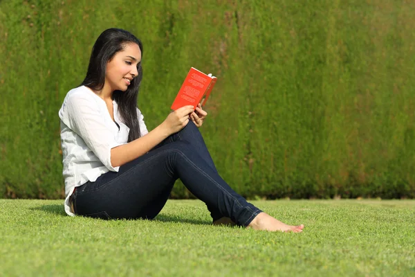 Mooie Arabische vrouw lezen van een boek zittend op het grasveld in het park — Stockfoto