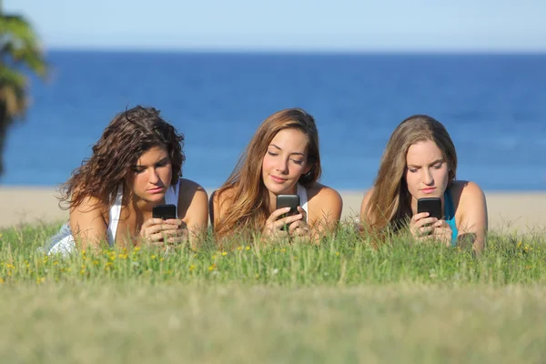 Grupo de três meninas adolescentes digitando no telefone celular deitado na grama — Fotografia de Stock