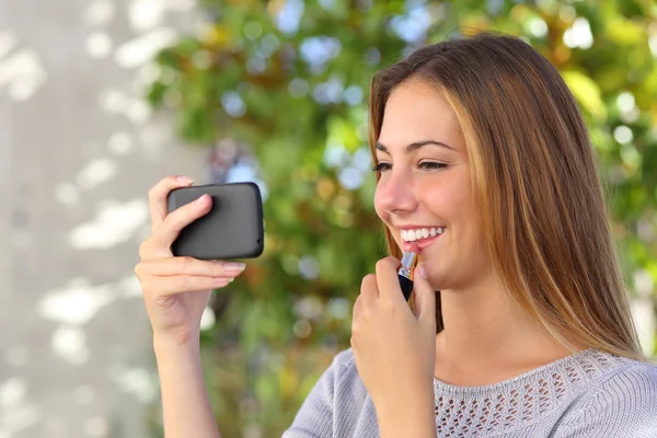 Schöne Frau, die ein Smartphone als Spiegel benutzt — Stockfoto