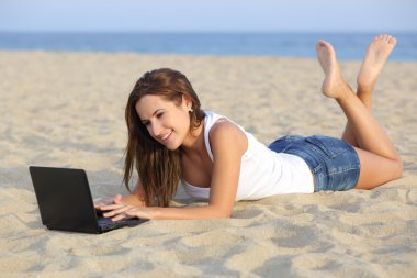 güzel genç kız plajın kumları üzerinde yalan onun netbook bilgisayar tarama