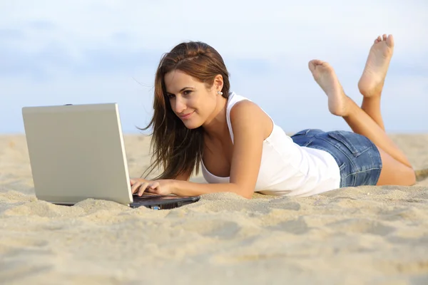 Vacker tonåring tjej beter hennes laptop liggande på sanden på stranden — Stockfoto