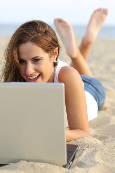 Вид спереди девочки-подростка, просматривающей свой ноутбук, лежащий на песке пляжа — стоковое фото