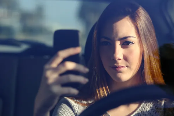 Vista frontal de una mujer conduciendo un coche y escribiendo en un teléfono inteligente — Foto de Stock