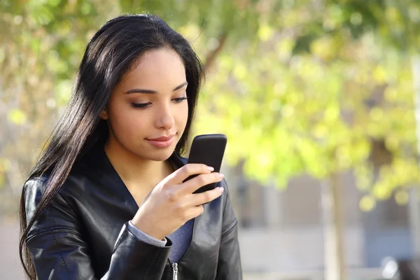 Mulher bonita mensagens de texto em um telefone inteligente em um parque — Fotografia de Stock