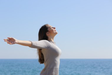 Happy woman breathing deep fresh air and raising arms on the beach clipart