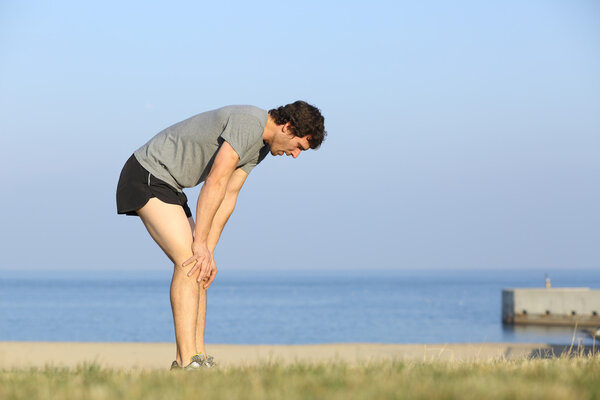 Exhausted runner man resting on the beach after workout