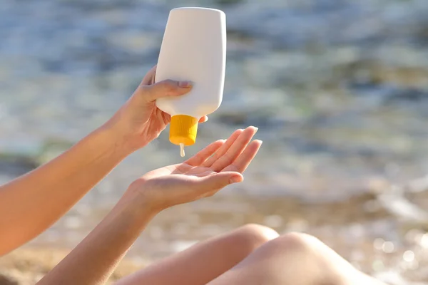 Vrouw handen zetten zonnebrandcrème uit een fles op het strand — Stockfoto