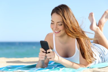 Sahilde yatan bir akıllı telefon kullanan güzel genç kız