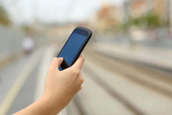 Mulher mão segurando um telefone inteligente em uma estação de trem — Fotografia de Stock