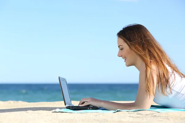 Side view of a teenager girl browsing a laptop on the beach Royalty Free Stock Images