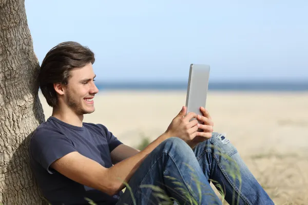 Lycklig man läser en tablett läsare sitter på stranden — Stockfoto