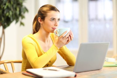 Sarı giyinmiş, laptopuyla kahve içen bir öğrenci eve bakıyor.