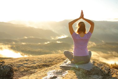 Güneş doğarken dağda yoga yapan bir kadının arka plan portresi.