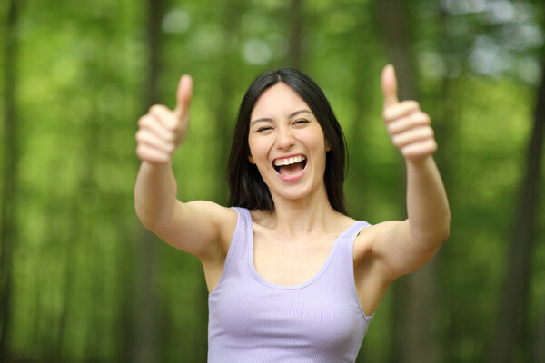Портрет счастливой азиатки, показывающей пальцами вверх в парке