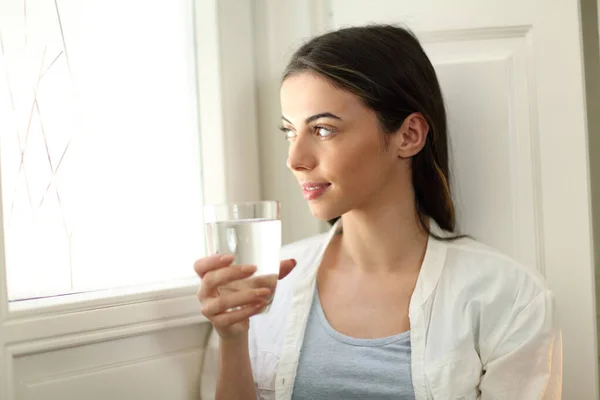 Mujer Feliz Sosteniendo Vaso Agua Asomándose Por Ventana Sentada Casa — Foto de Stock