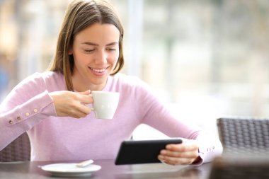 Akıllı telefondan medyayı izleyen mutlu kadın bir barda içki içiyor.