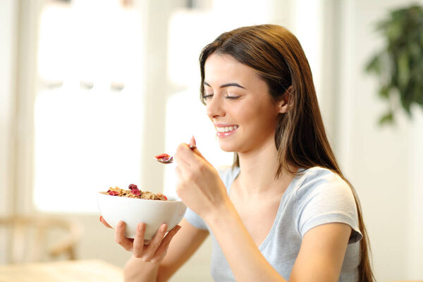 Happy woman holding a bowl and spoon eating cereals sitting at home