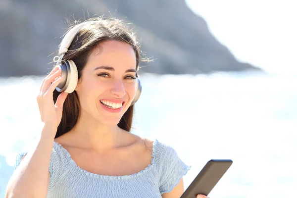 Счастливая Женщина Слушает Музыку Держа Наушники Телефон Глядя Камеру Пляже — стоковое фото