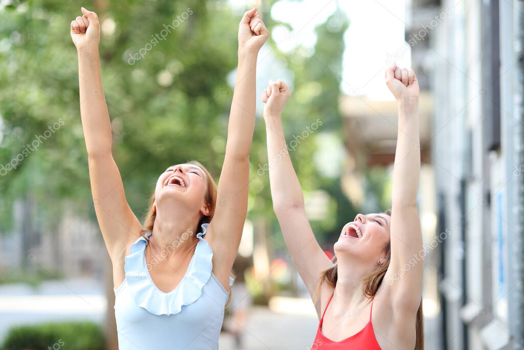 Happy friends raising arms celebrating success in the street