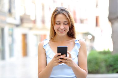 Sokakta akıllı telefon kullanarak yürüyen mutlu bir kadının portresi.