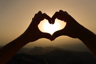 Bir kadının arka ışığını kapat eller siluet çerçeve güneş kalp şeklinde