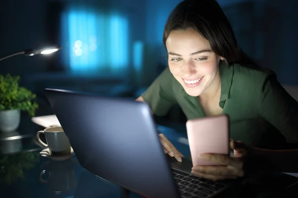 Happy Woman Night Home Using Laptop Checking Smart Phone — Fotografia de Stock