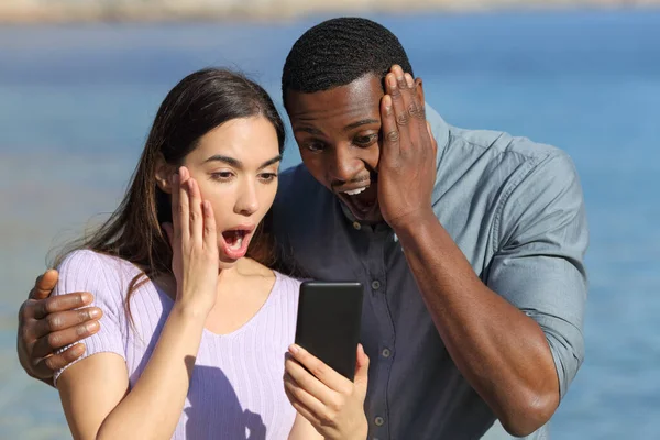 Sorprendida Pareja Interracial Comprobando Teléfono Inteligente Playa Vacaciones —  Fotos de Stock