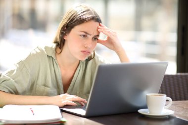 Frustrated student checking online content on laptop in a coffee shop