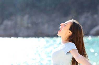 Excited woman celebrating screaming on the beach on summer vacation