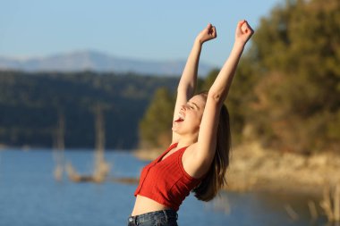 Kırmızı elbiseli heyecanlı kadın tatilini doğada çığlık atarak kutluyor.